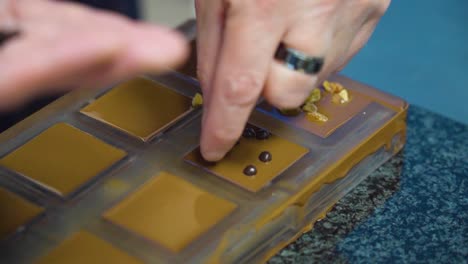 topping chocolate squares with nuts and dried fruits by hand