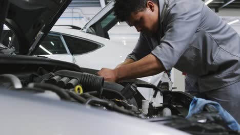 mecánico de automóviles afroamericano mirando un motor de automóvil abierto y comprobando si algo está roto