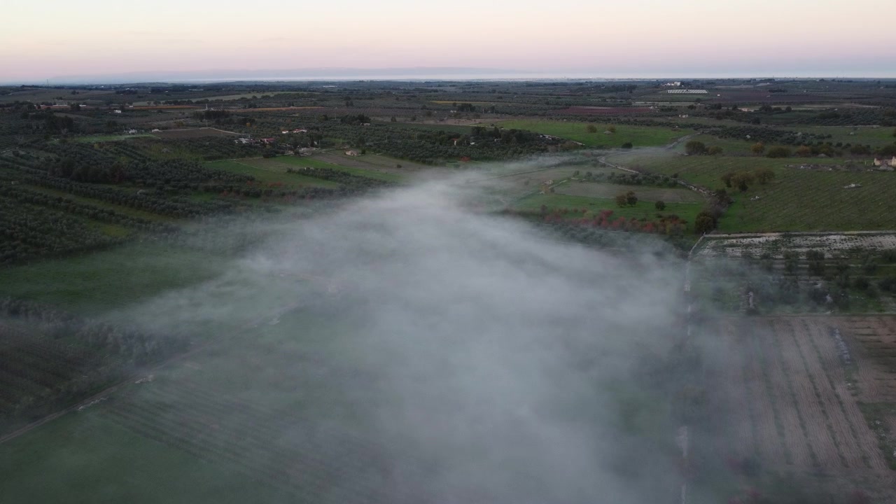 Ripresa aerea con drone sopra fumo atmosferico e nebbia che scorrono tra vigneti, campi arati e uliveti al tramonto in Puglia, Italia. Paesaggio suggestivo. Video 4K cinematografico