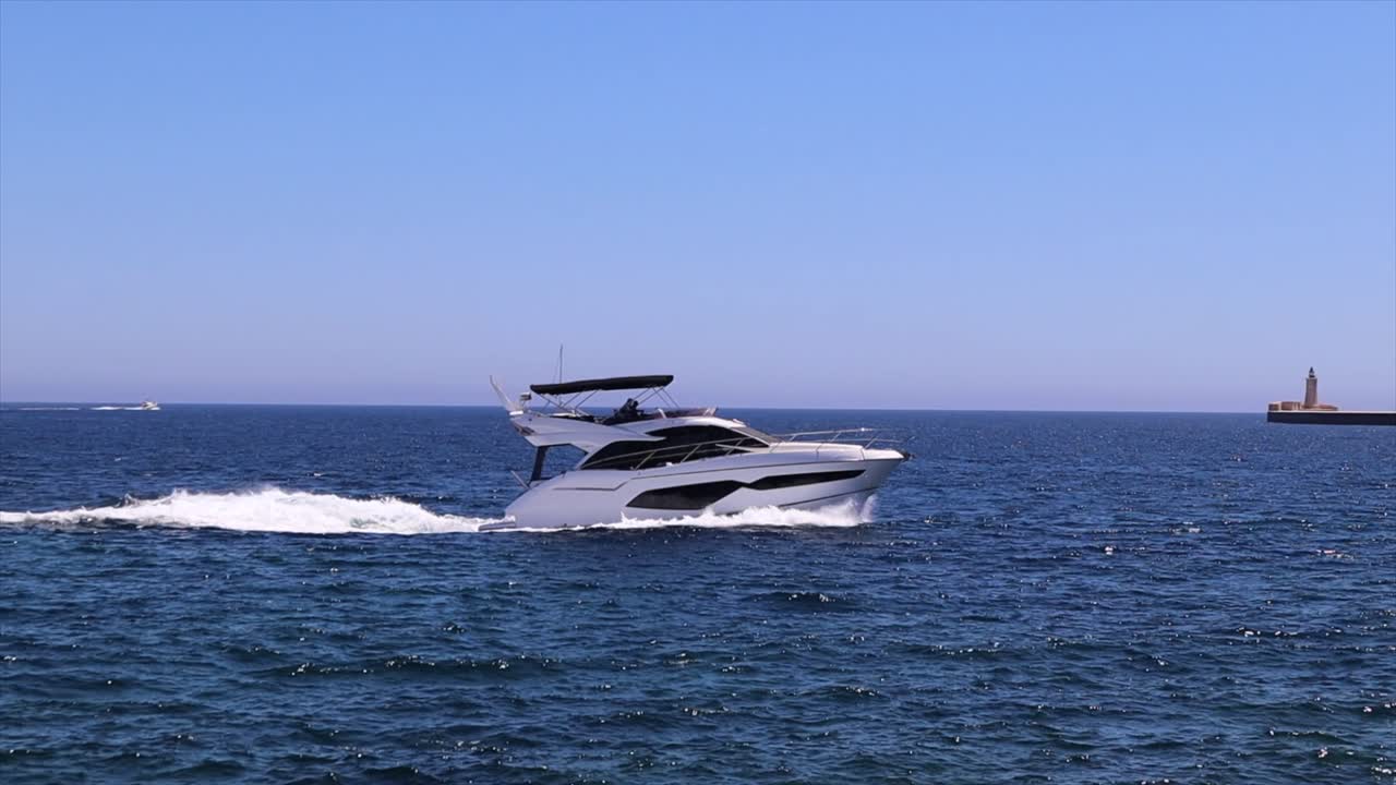 yate de motor de lujo navegando rápido en el mar azul con el rompeolas de valletta en el fondo, cámara lenta