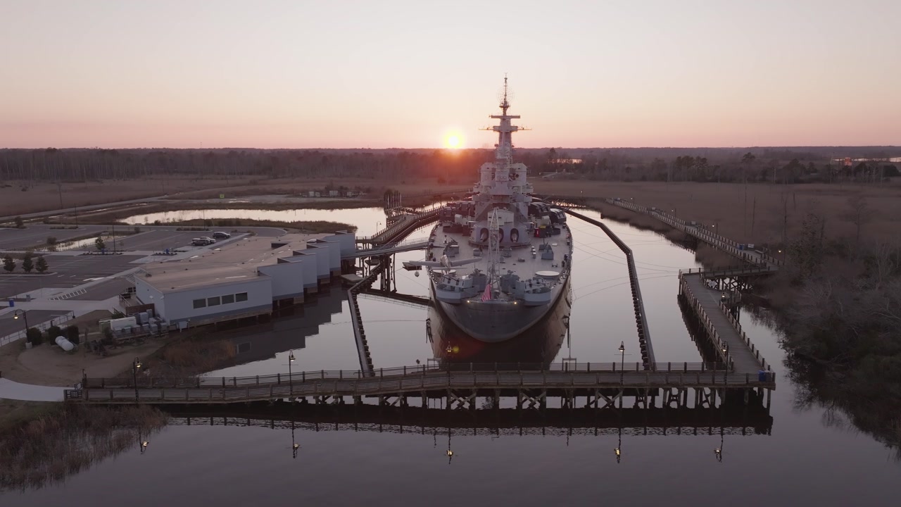 4k drone shot tracking around a North Carolina battleship at sunset near a coastal town