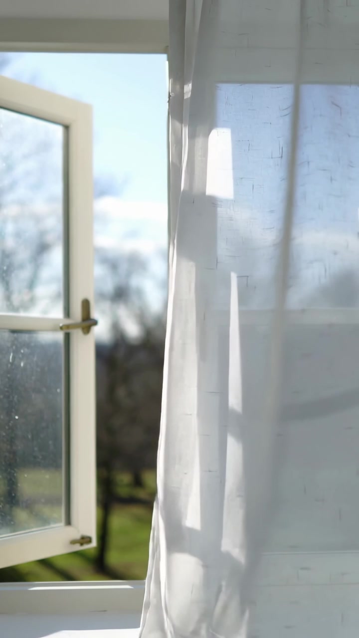 Vertical video: Swaying drape inward in room, breeze entering left window, sunlight casting shadows