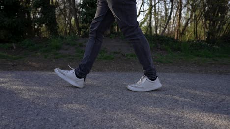 close up of man legs walking on paved street with trees in background