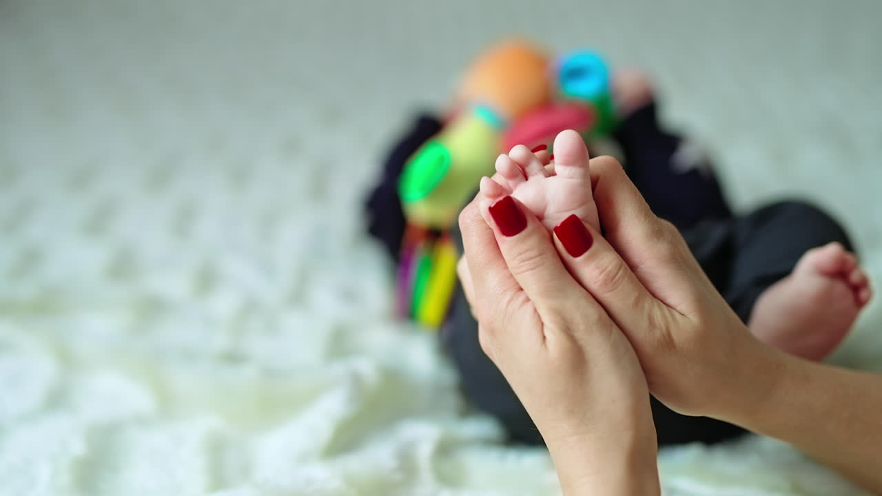 Mother massaging her baby's tiny foot with her thumbs. Little kid trying to take his legs away. Close up. Blurred backdrop.