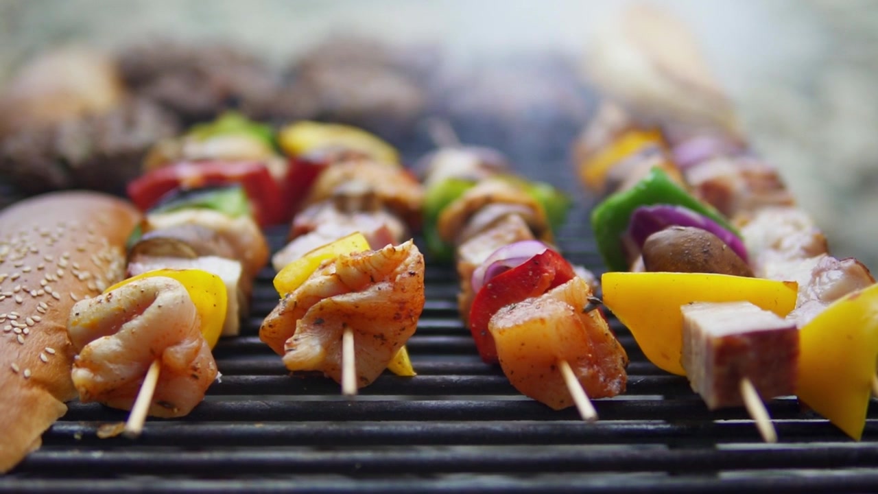 Primo piano di spiedini sfrigolanti di pollo e verdure che grigliano all'aperto, catturato con profondità di campo ridotta e luce naturale per un filmato di barbecue appetitoso