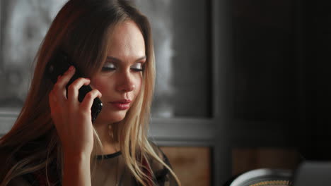 young smiling hipster girl talking with friend via video call via laptop computer while sitting in coffee shop. cheerful female manager having webinar via portable notebook during resting time in cafe