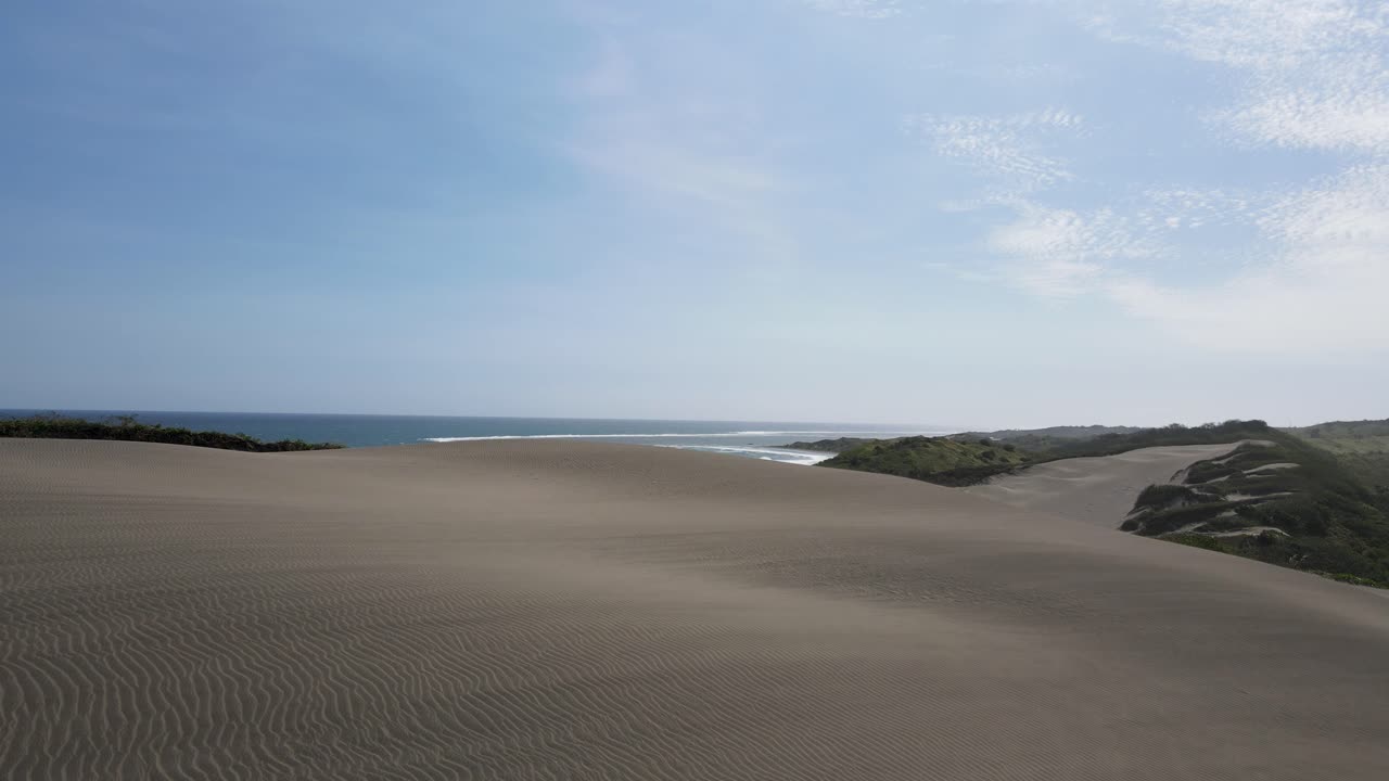 vista cinematográfica a través del paisaje natural de dunas de arena que conducen a las olas del océano que chocan contra la orilla de la playa del paraíso