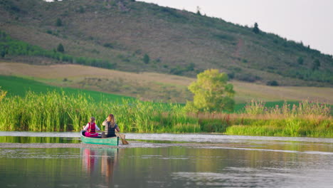 two people canoeing on a tranquil lake with a scenic hillside backdrop