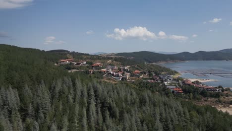 a scenic aerial shot of a small village nestled in the hills next to a reservoir, surrounded by forest and mountains