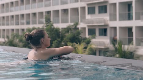 lady in black bikini swims against long high resort hotel