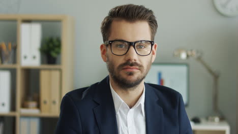 Retrato-Del-Apuesto-Joven-Con-Gafas,-Camisa-Y-Chaqueta-Sonriendo-A-La-Cámara-En-Su-Oficina