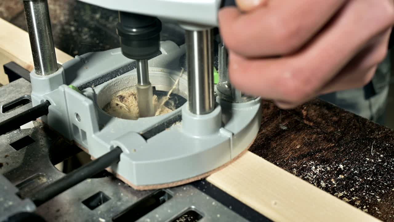 가정 작업실에서 수동 전기 절단기로 작업하는 목수의 손의 클로즈업입니다.