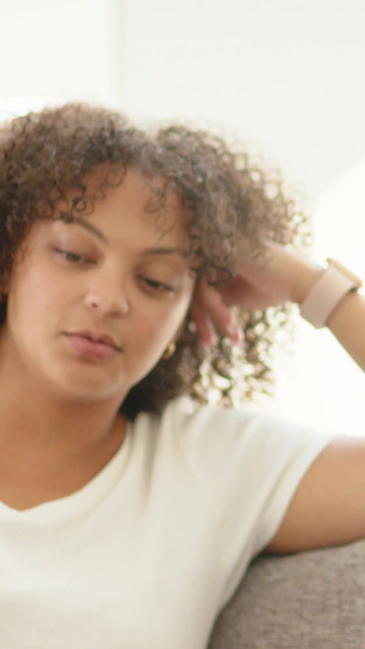 Vertical video: Panning showing curly woman speaking on couch for vlog with ring light, smartwatch