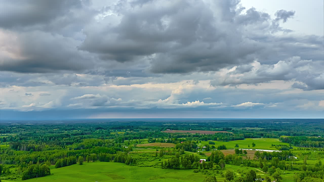 White cumulus clouds drift over meadows and forests in a panoramic aerial view