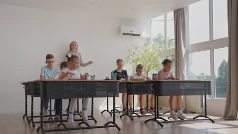 de kinderen in de klas zitten aan hun bureau en de leraar loopt door de klas en legt het onderwerp van de les uit. slimme kinderen leren in een vriendelijke moderne omgeving