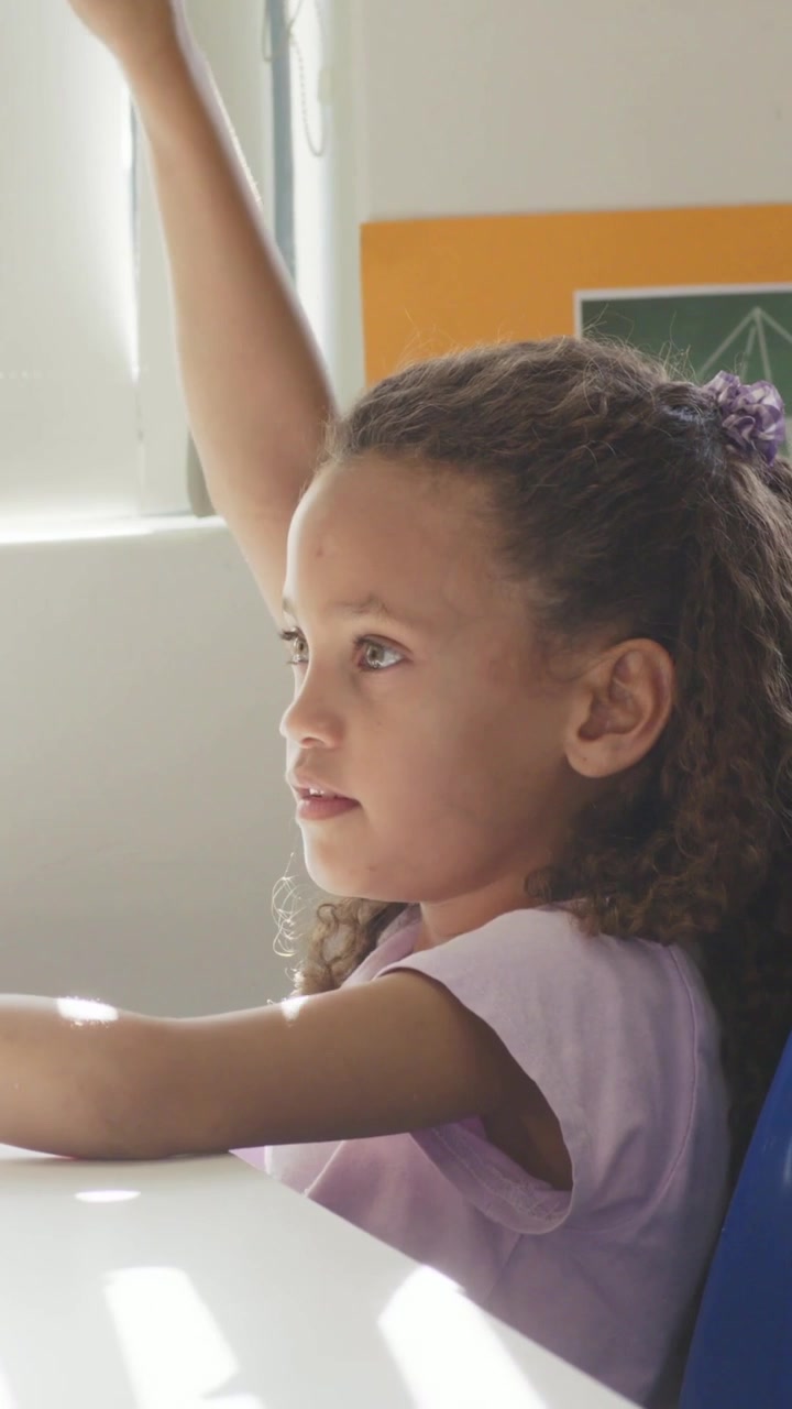 Vertical video: Responding to off-frame cue, student in purple shirt raising hand at table, blinds