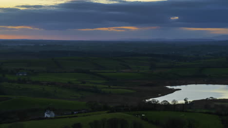 time lapse of rural farming landscape of farmhouse at lake in grass fields and hills during dramatic cloudy sunset viewed from keash caves in county sligo in ireland