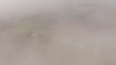 aerial drone moves through clouds above grassland and farmland in midwest of united states