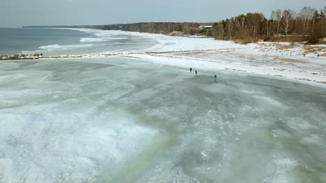 Antena-De-Gente-Caminando-Sobre-Hielo,-Orilla-Del-Mar-Medio-Congelada---Toma-De-Drones