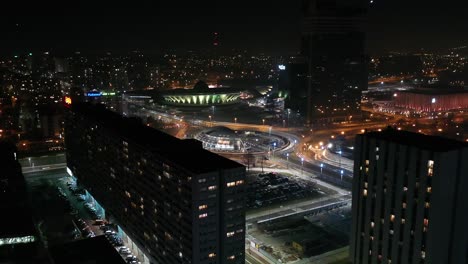 Aerial-drone-view-of-the-center-of-Katowice,-The-roundabout-Generała-Ziętka-and-Superjednostka-in-foreground---Day-to-night-transition