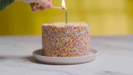 studio shot birthday cake covered with decorations and single candle being lit 3