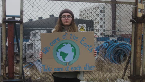 jovem ativista feminina segurando um cartaz de papelão durante um protesto contra as mudanças climáticas enquanto olha para a câmera