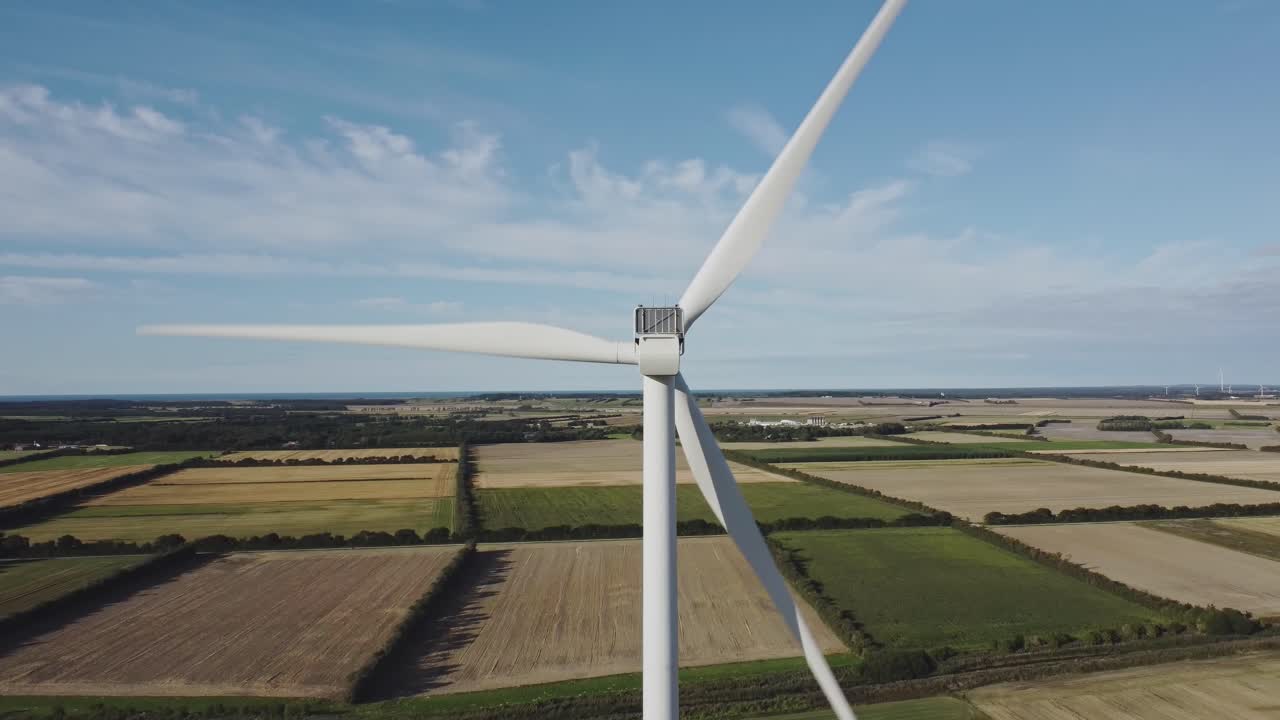 лопасти ротора ветряной турбины вращаются на фоне растущих на полях культур в светлое время суток