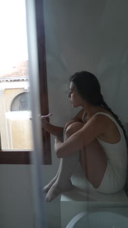 woman brushing teeth by the window