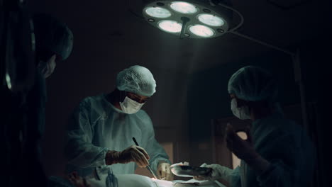 medical staff performing surgical operation in dark hospital emergency room.