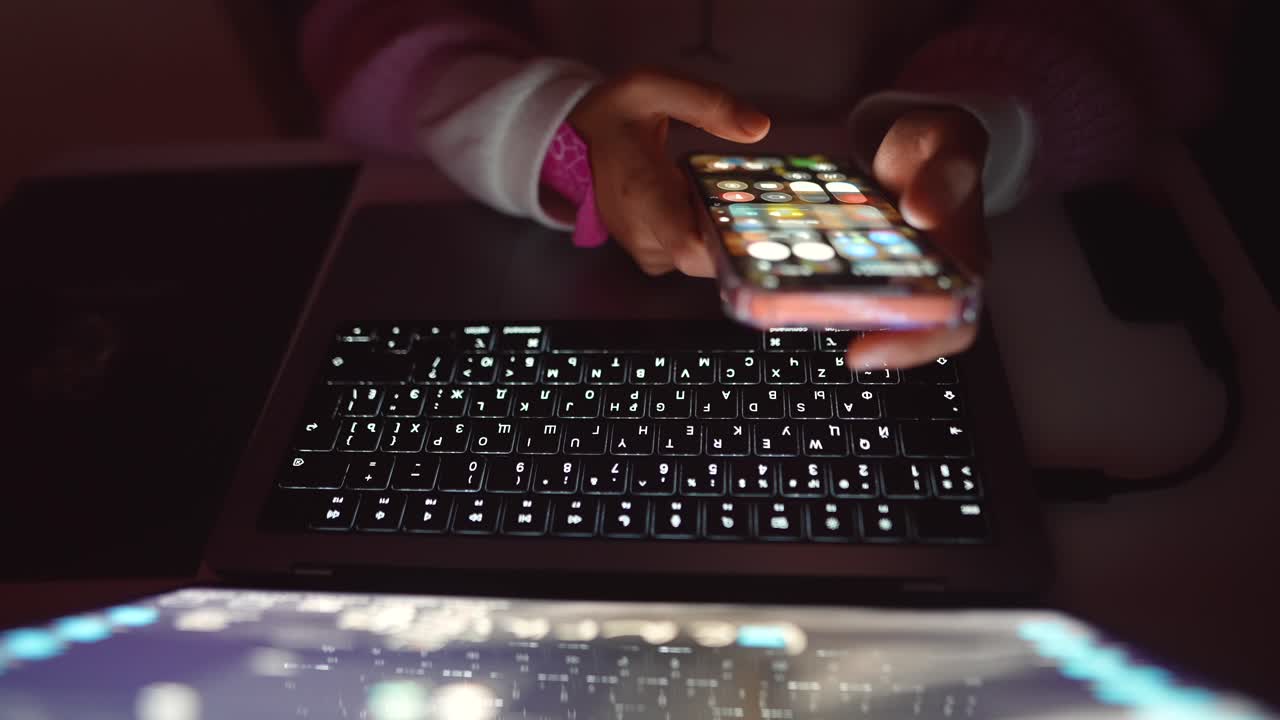 Persona che usa un laptop e un telefono cellulare al buio