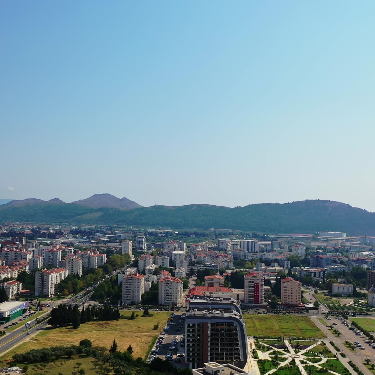 Scenic view of the city at the coast of Adriatic Sea. Green mountain ranges at backdrop. Sunny day footage from drone