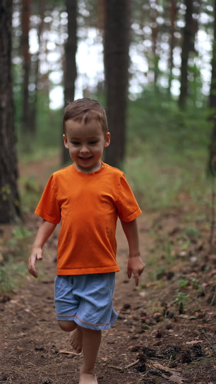 Active happy kid approaching camera. Lovely kid runs barefoot by the path in the forest. Vertical video.