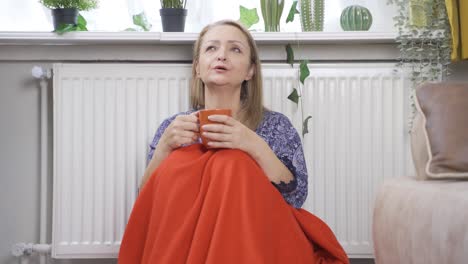 the woman drinking coffee leaning against the heater is cold.