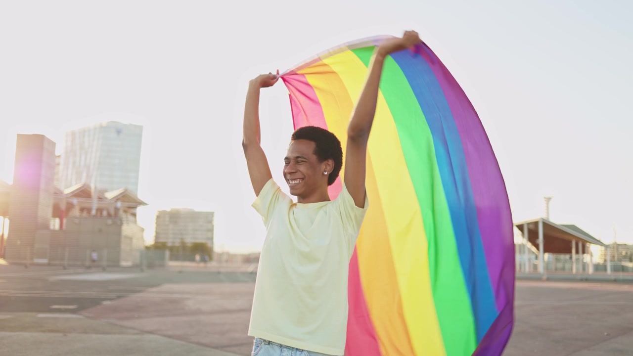 Proud Young Man Waving LGBTQ+ Rainbow Flag at Sunset