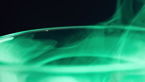 macro of the edge of a glass above which green smoke flows and rises