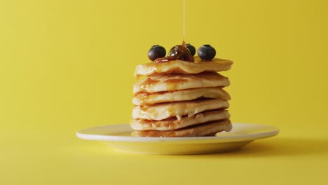 Video-Von-Ahornsirup,-Der-In-Pfannkuchen-Auf-Gelbem-Hintergrund-Gegossen-Wird