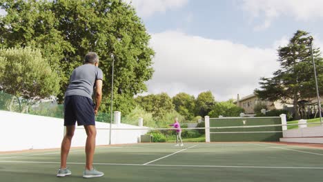 Video-of-biracial-senior-man-playing-tennis-on-tennis-court