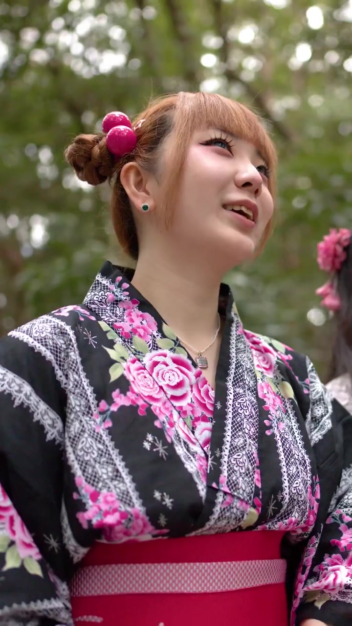 Mladá Japonka v květinovém kimonu se usmívá, zatímco stojí v bujném lese.