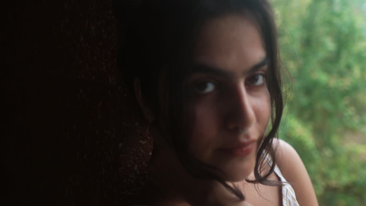 retrato de una mujer con una expresión serena, apoyada en una pared y mirando directamente a la cámara, en un fondo natural borroso