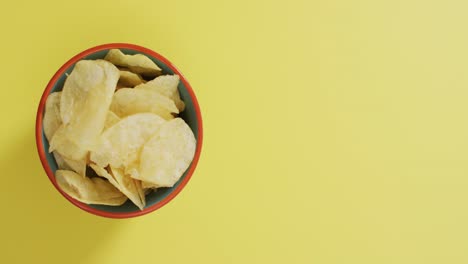 Close-up-of-potato-chips-in-a-bowl-with-copy-space-on-yellow-surface