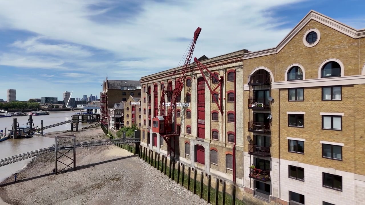 Røde lastkraner står op imod den gule murstensfacade på en historisk flodkaj, der er omdannet til lejligheder.