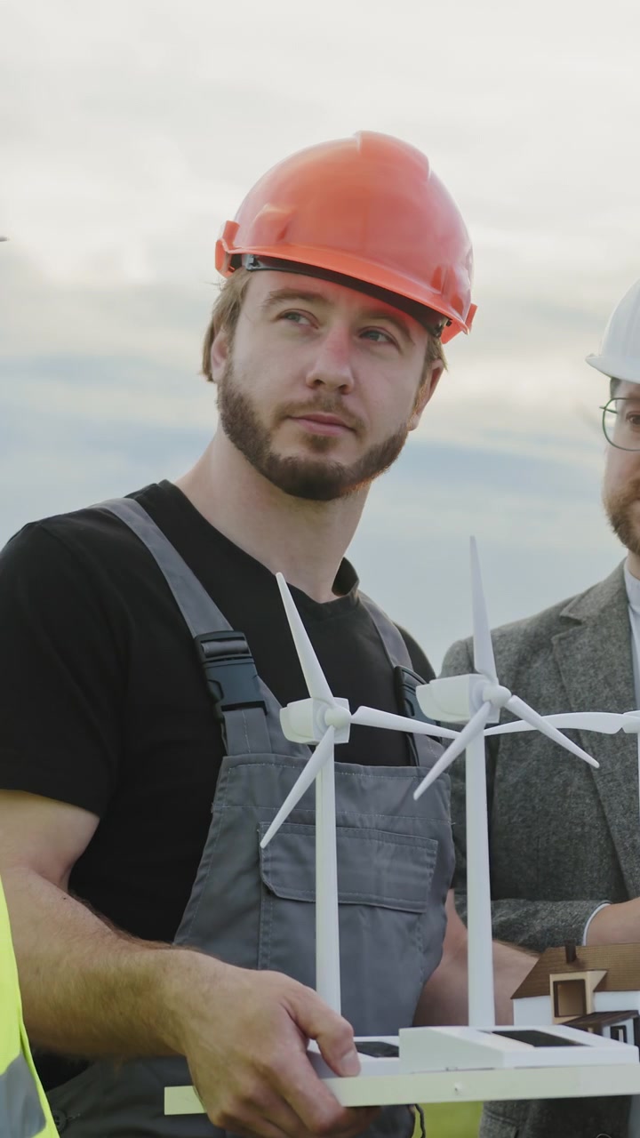 Engineers examine wind turbine and house models discussing sustainable development and clean energy