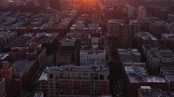 Dramatischer stationärer Tilt-up aus der Luft über das Harlem-Viertel von New York City, der einen wunderschönen Sonnenaufgang mit Lens Flare enthüllt.