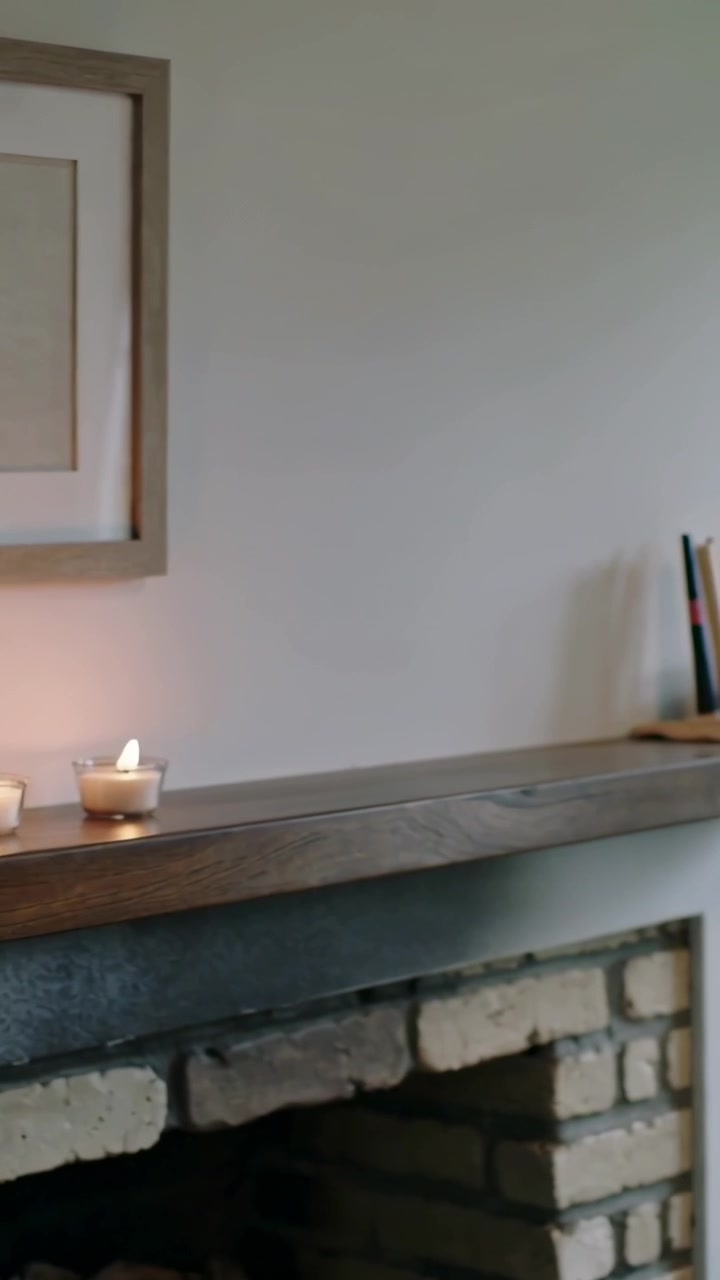 Vertical video: Hands reaching lighting three tealights on mantel, view panning to books for decor