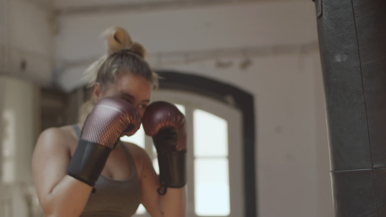 Mezzo busto di una seria kickboxer che colpisce un sacco da boxe.