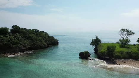 a young man is standing on the edge of a small cliff, looking down in the crystal clear water on a tiny islet outside lombok, indonesia