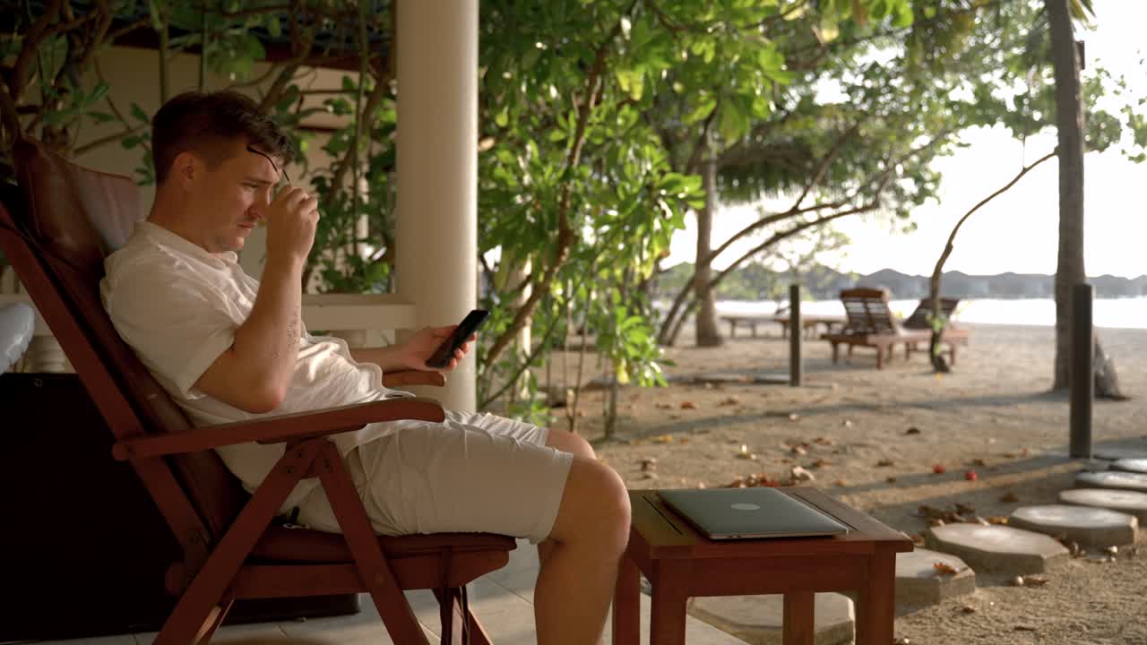 해변 의자에서 스마트폰으로 뉴스를 스크롤하는 남자.