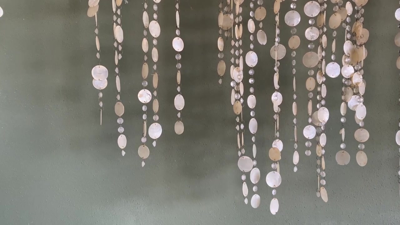 Shell wind chimes swaying gently in the breeze against green wall background. 4K.