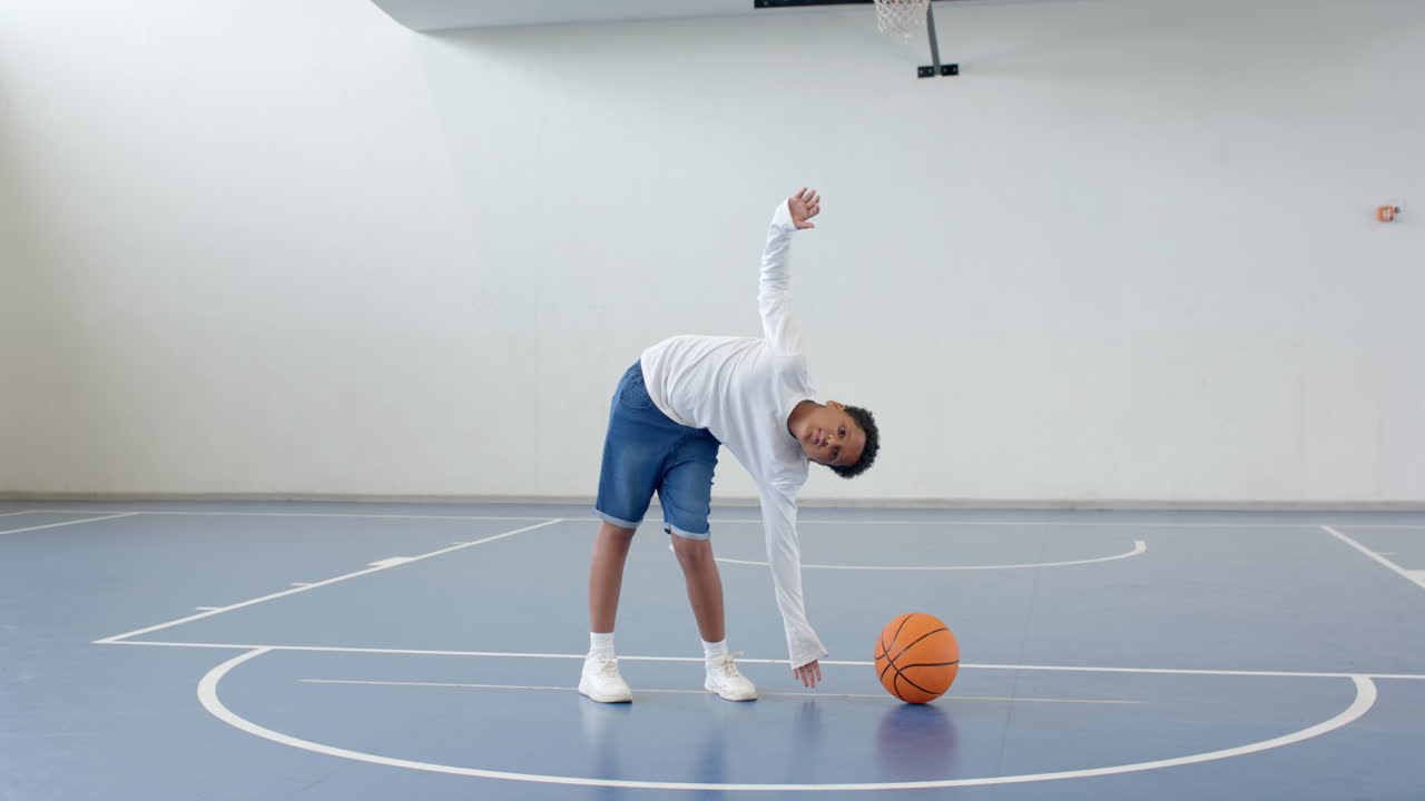 Boy stretching on basketball court with ball, preparing for practice, copy space