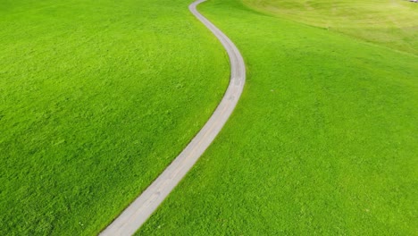 Serene-road-on-meadow-leading-to-idyllic-Egg-village,-Switzerland,-aerial-tilt-up-reveal